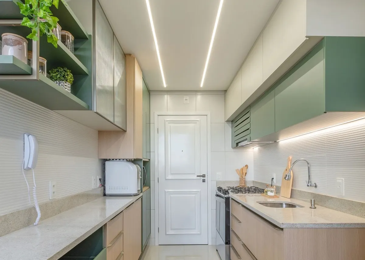 Cozinha em corredor com armários verdes e iluminação linear no teto