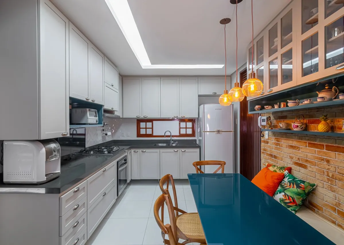 Cozinha com bancada azul, armários brancos e mesa de refeições