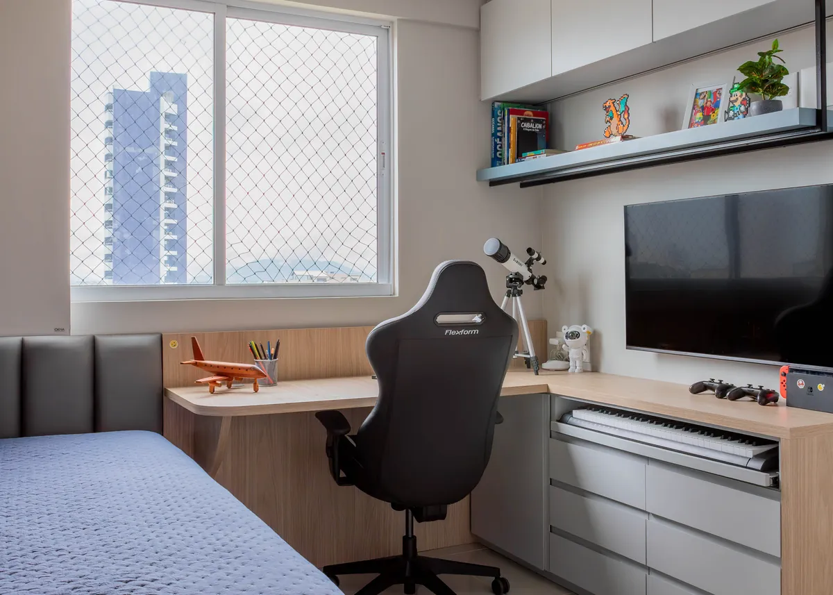 Quarto de adolescente com cama azul, bancada de estudo junto à janela e prateleiras iluminadas