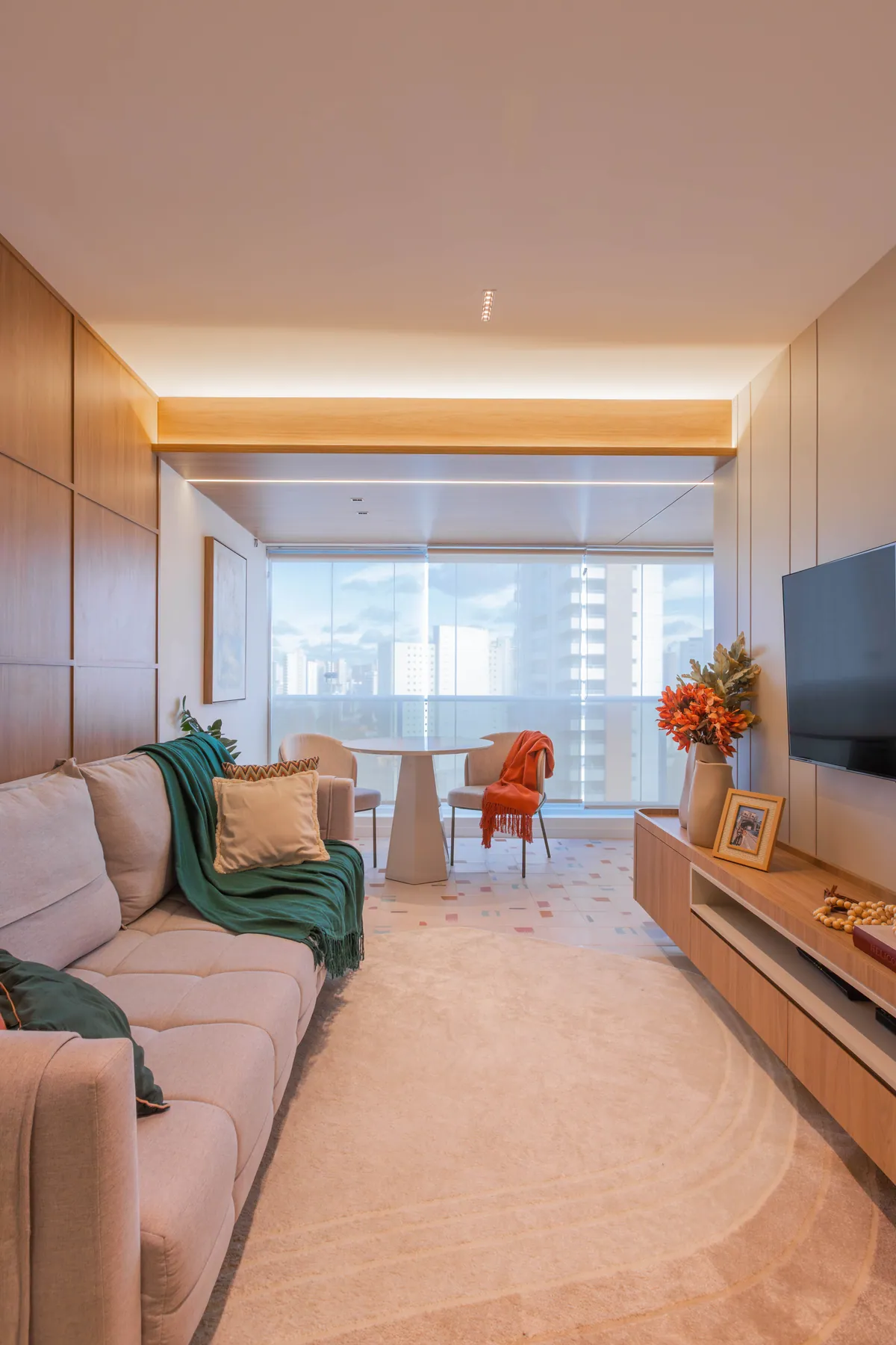 Estar do Apartamento Blue: sofá claro com manta verde, poltrona terracota e painel de madeira com TV