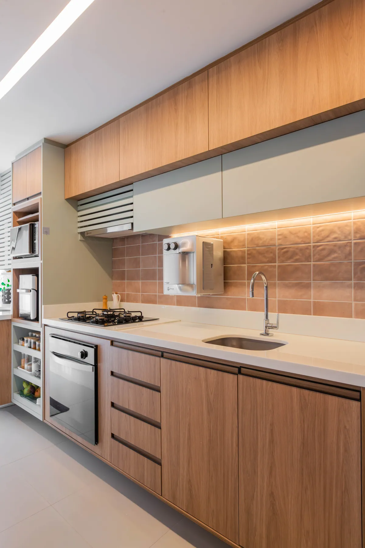 Cozinha do Apartamento Blue em corredor, com marcenaria de madeira clara e revestimento terracota